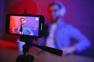 vlogger using smartphone to film podcast in studio. blogger with mobile phone, microphone and headphones filming for social media broadcasting career. photo