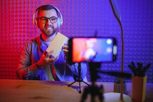 Male technology blogger recording blog or vlog review of new smartphone, showing it on camera at home studio. Blogging, Work from Home concept. Selective focus. Web Banner photo