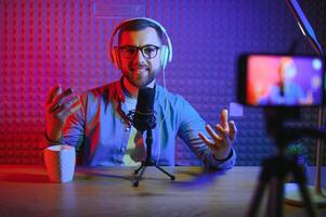 vlogger using smartphone to film podcast in studio. blogger with mobile phone, microphone and headphones filming for social media broadcasting career. photo