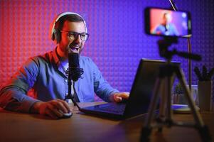 Young man recording or streaming podcast using microphone at his small broadcast studio. Content creator. photo
