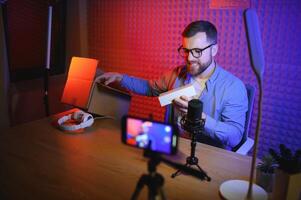 Panoramic view of young adult vlogger creating internet content, holding carton box in hands, unpacking received pack and recording media online on broadcast equipment photo