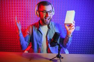 Male technology blogger recording blog or vlog review of new smartphone, showing it on camera at home studio. Blogging, Work from Home concept. Selective focus. Web Banner photo