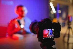 Male technology blogger recording blog or vlog review of new smartphone, showing it on camera at home studio. Blogging, Work from Home concept. Selective focus. Web Banner photo