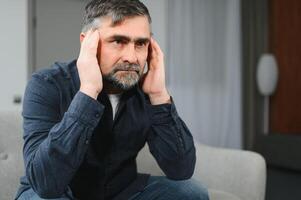 Closeup of middle-aged bearded man suffering from headache at home, touching his temples, panorama with copy space. Migraine, headache, stress, tension problem, hangover concept photo