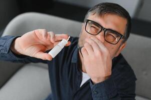 Illness And Sickness. Closeup Of man Feeling Sick Dripping Nasal Drops In Blocked Nose. Portrait male Sprays Cold And Sinus Medicine In Runny Nose. Sinusitis treatment photo