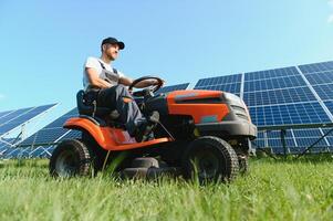 A man drives a lawnmower near solar panels. Concept of solar energy photo