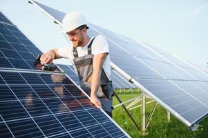 Side view of male worker installing solar modules and support structures of photovoltaic solar array. Electrician wearing safety helmet while working with solar panel. Concept of sun energy photo