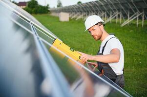 Side view of male worker installing solar modules and support structures of photovoltaic solar array. Electrician wearing safety helmet while working with solar panel. Concept of sun energy photo