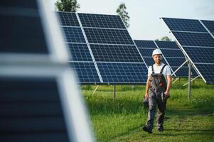 Side view of male worker installing solar modules and support structures of photovoltaic solar array. Electrician wearing safety helmet while working with solar panel. Concept of sun energy photo