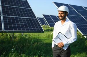 Portrait of Young indian male engineer standing near solar panels, with clear blue sky background, Renewable and clean energy. skill india, copy space. photo