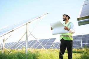 Portrait of Young indian male engineer standing near solar panels, with clear blue sky background, Renewable and clean energy. skill india, copy space. photo