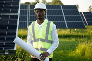 Close up portrait of young african american engineer worker in hardhat holding solar plan. Green electricity future concept. photo