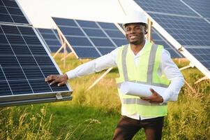 Close up portrait of young african american engineer worker in hardhat holding solar plan. Green electricity future concept. photo