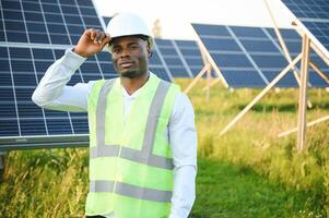 Close up portrait of young handsome African American craftsman a protective helmet. Happy man in overalls posing at camera smiling. Slow motion. photo