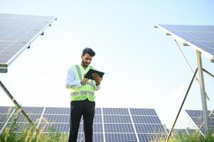 Portrait of Young indian male engineer standing near solar panels, with clear blue sky background, Renewable and clean energy. skill india, copy space. photo