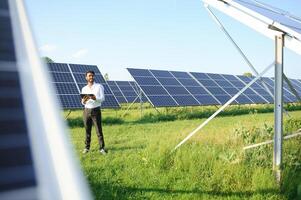 Portrait of Young indian male engineer standing near solar panels, with clear blue sky background, Renewable and clean energy. skill india, copy space. photo