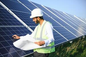 Portrait of Young indian male engineer standing near solar panels, with clear blue sky background, Renewable and clean energy. skill india, copy space. photo