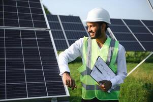 Portrait of Young indian male engineer standing near solar panels, with clear blue sky background, Renewable and clean energy. skill india, copy space. photo