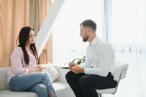 Psychologist taking notes during therapy session with sad young woman in his office. Copy space photo