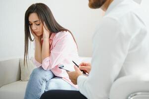 Psychologist taking notes during therapy session with sad young woman in his office. Copy space photo