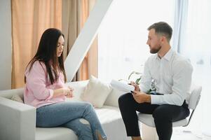 Psychologist taking notes during therapy session with sad young woman in his office. Copy space photo