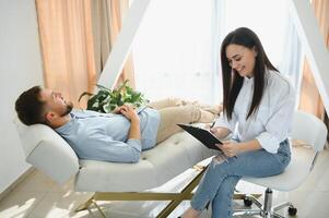 Depressed man speaking to a therapist while she is taking notes photo