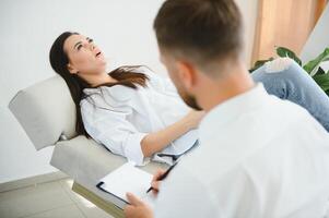 Psychologist taking notes during therapy session with sad young woman in his office. Copy space photo