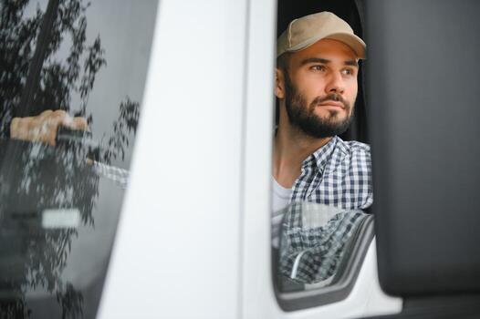 A driver sitting inside the semi-truck while looking through the open window with multiple trucks parked in the background photo