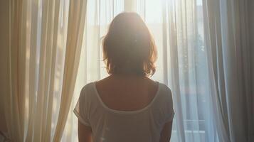 Woman Looking Out Window at Sunset With Sheer Curtains photo