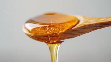 Golden Honey Dripping From Wooden Spoon Against White Background in Bright Natural Light. photo
