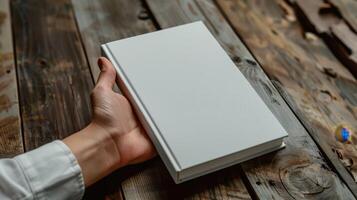 A Person's Hand Resting on a Blank Book Against a Rustic Wooden Surface photo