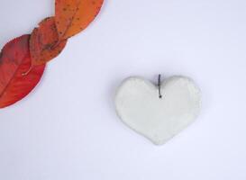 White handmade heart and bright fallen autumn leaves on white paper sheet background photo