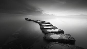 Tranquil sunset ocean landscape with rocks fading into the horizon in black and white photo