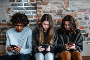 Three students sitting against brick wall using smartphones photo