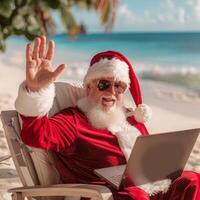Santa claus waving and working on laptop at the beach photo