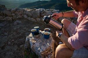 Man pouring coffee from thermos, enjoying outdoor adventure with scenic mountain view photo