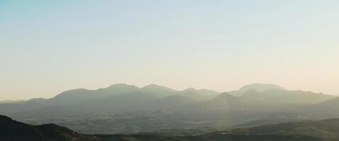 Panoramic view of serene mountain range at sunrise with mist and soft light photo