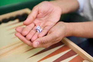 Hands holding dice by a backgammon board, ready for a game photo