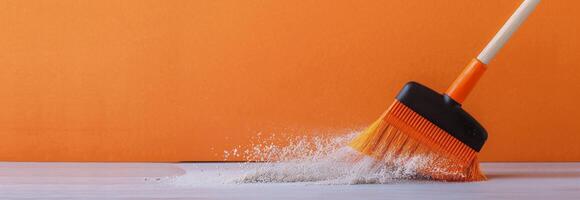 Broom Sweeping Dust on Wooden Surface With Orange Background photo