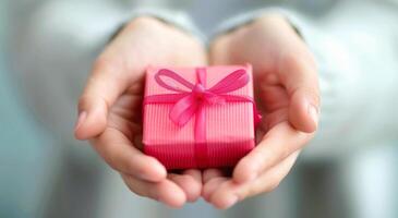 Gift Wrapped in Pink Ribbon Presented by Hands in Soft Light photo