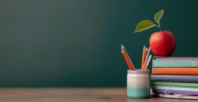 Red Apple and Colorful Pencils on Stacked Books Against a Green Wall photo