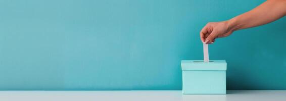 Hand Inserting Ballot Into Light Blue Box Against Teal Background photo
