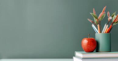 Red Apple and Colorful Pencils on Stacked Books Against a Green Wall photo