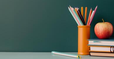 Red Apple and Colorful Pencils on Stacked Books Against a Green Wall photo