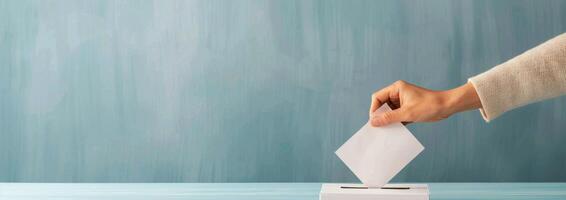 Hand Inserting Ballot Into Light Blue Box Against Teal Background photo
