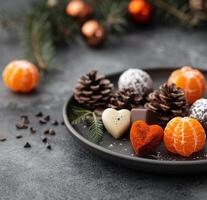 Tangerines, Chocolate, and Pine Cones on a Dark Surface photo
