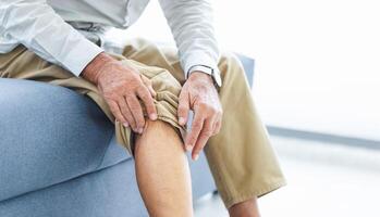 Senior man suffering from knee pain while sitting on the sofa, Old man suffering from knee pain sitting sofa photo