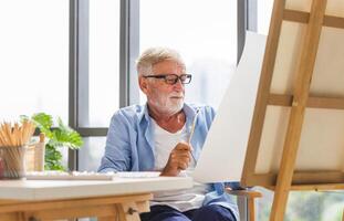 Caucasian senior man painting on canvas at home, Elderly man painting on a canvas, Happy retirement concepts photo