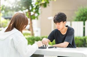 Mother playing chess with a son, Asian family relaxing hobbies playing chess in a park photo