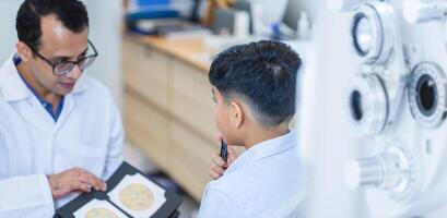 Boy doing eye test checking examination with optometrist in optics store, Indian kid boy choosing eyeglasses in optics store, Optometrist doing color blindness disease perception test in optical shop photo